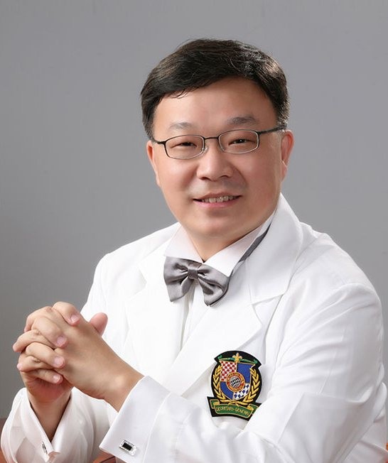 김진왕 대표원장 — 흰 가운·나비넥타이·가슴 엠블럼, 깍지 낀 손, 회색 배경